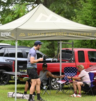 Auf einem Sportevent steht ein oliv-farbener, bedruckter Faltpavillon Serie E1 der Größe 3 x 3 Meter von Human Powered Movement.